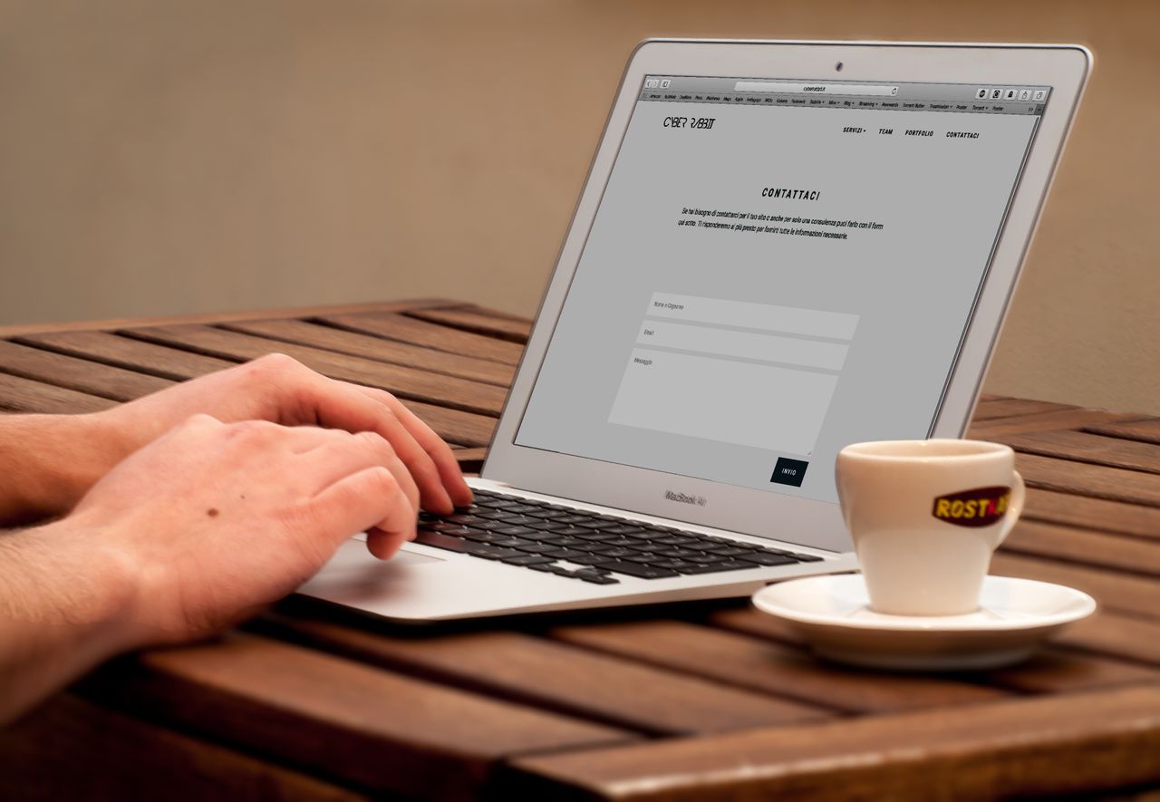 Vue rapprochée de mains tapant sur un ordinateur portable, à côté d'une tasse de café posée sur un bureau en bois.