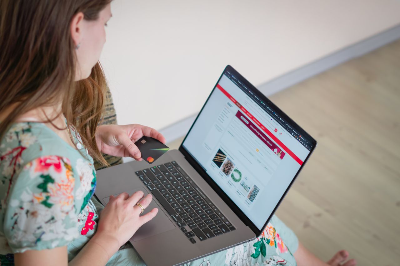 Woman in a floral dress shopping online with a laptop and credit card indoors.